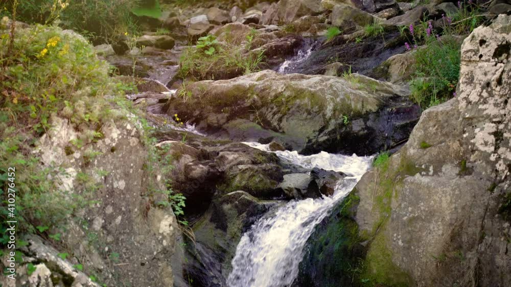 Waterfall and stream over rocks in green forest. Creek flows among rocks Waterfall and stream over rocks in green forest. Creek flows among rocks