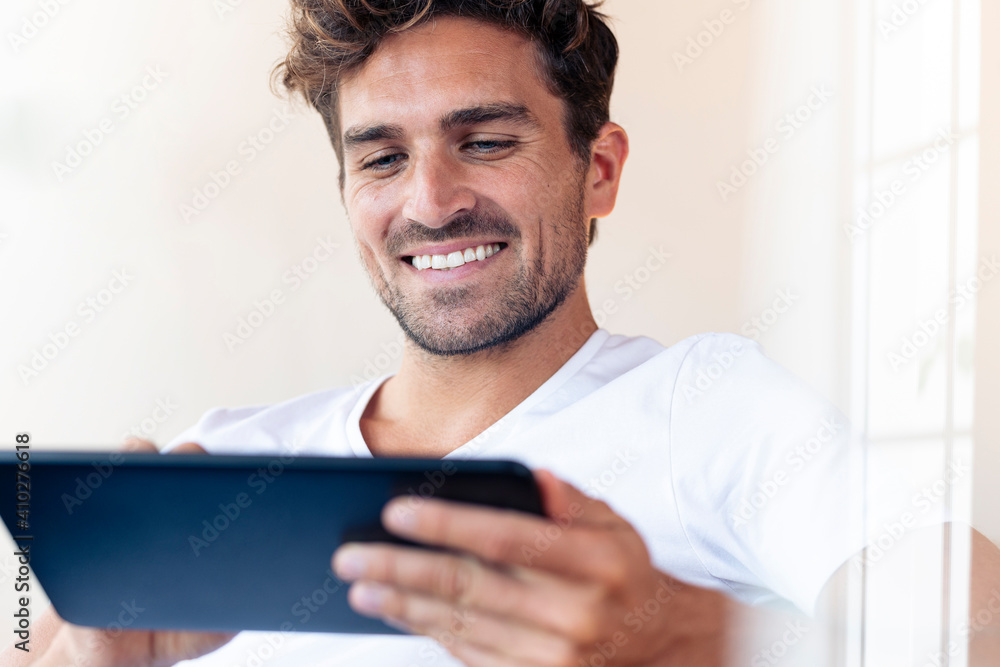 Mid adult man smiling while using digital tablet at home Mid adult man smiling while using digital tablet at home
