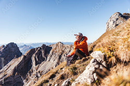 Male hiker contemplating while sitting on mountain against clear sky during sunny day