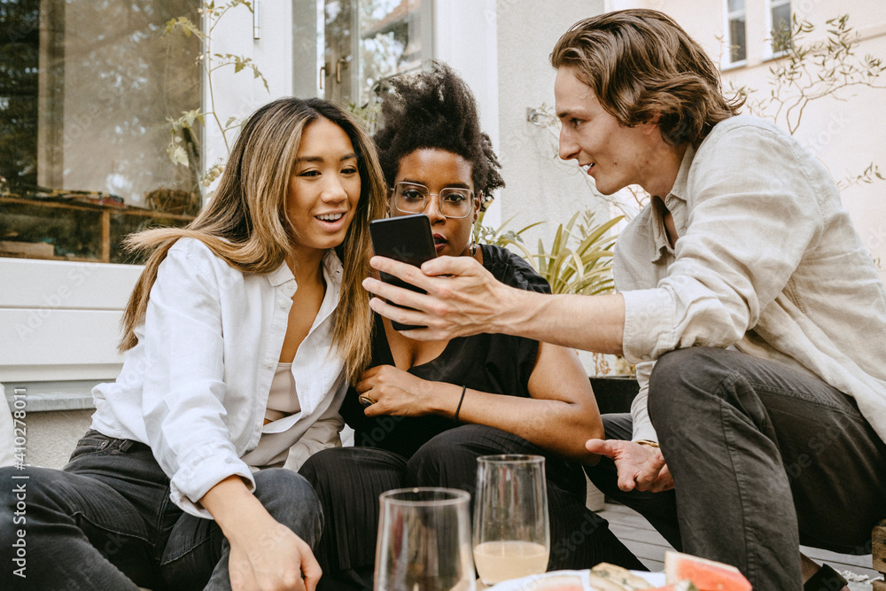 Man showing mobile phone to female friends in backyard Man showing mobile phone to female friends in backyard