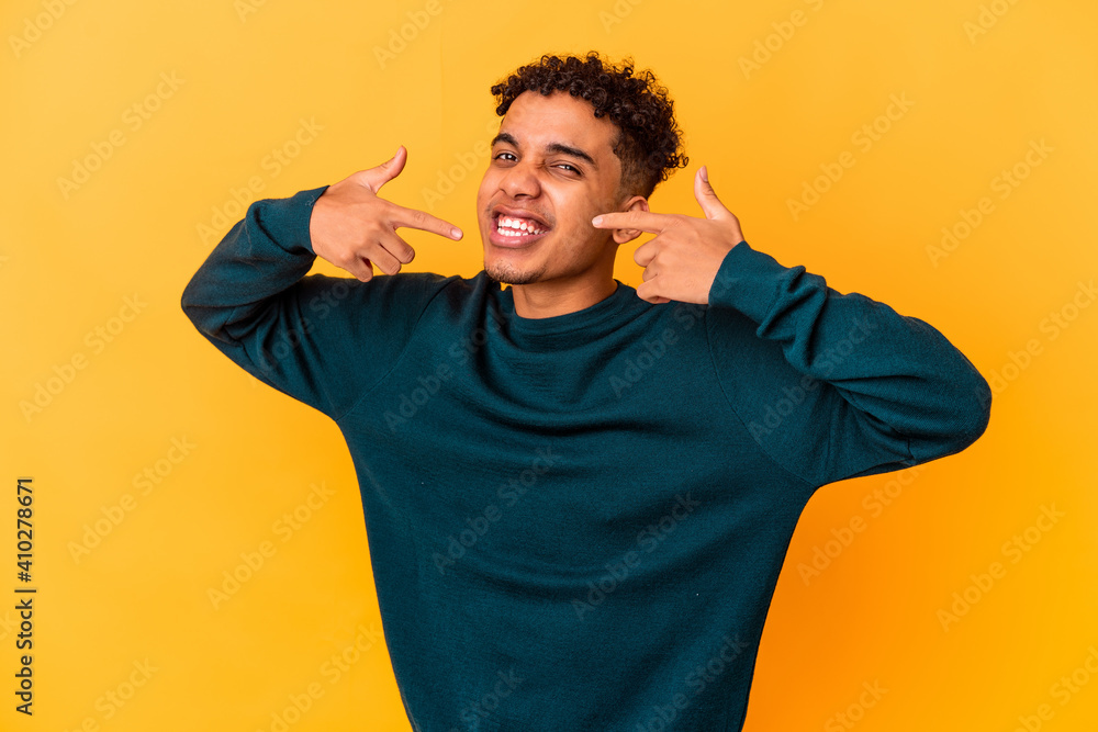 Young african american curly man isolated on purple smiles, pointing fingers at mouth. Young african american curly man isolated on purple smiles, pointing fingers at mouth.