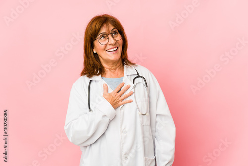 Middle age caucasian doctor woman isolated laughs out loudly keeping hand on chest.