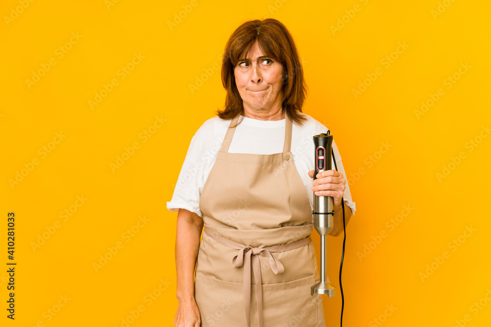 Middle age caucasian cook woman holding a mixer isolated confused, feels doubtful and unsure.