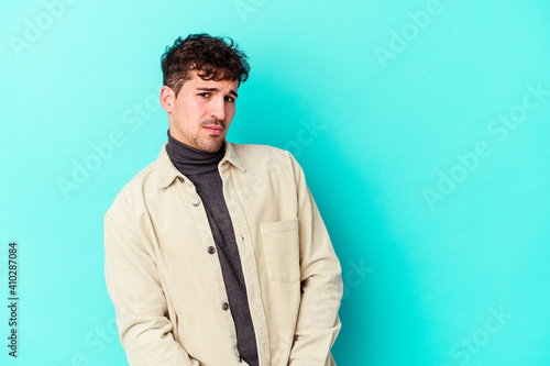 Young caucasian man isolated on blue background looks aside smiling, cheerful and pleasant.