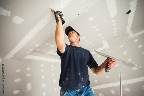 Drywall worker taping and mudding joint in ceiling photo