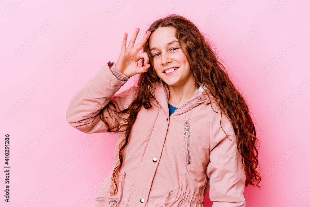 Little caucasian girl isolated on pink background winks an eye and holds an okay gesture with hand. Little caucasian girl isolated on pink background winks an eye and holds an okay gesture with hand.