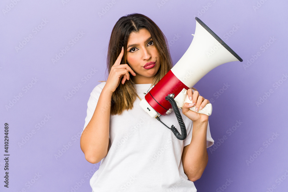 Young indian woman holding a megaphone isolated pointing temple with finger, thinking, focused on a task. Young indian woman holding a megaphone isolated pointing temple with finger, thinking, focused on a task.