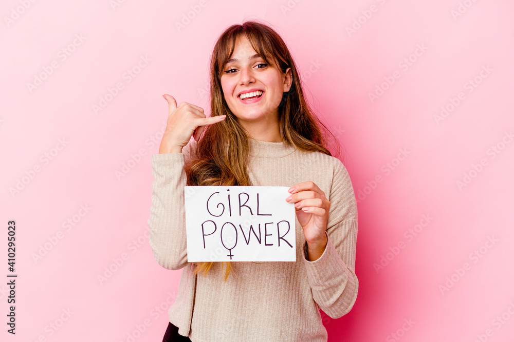 Young caucasian woman holding a girl power placard isolated on pink background showing a mobile phone call gesture with fingers.