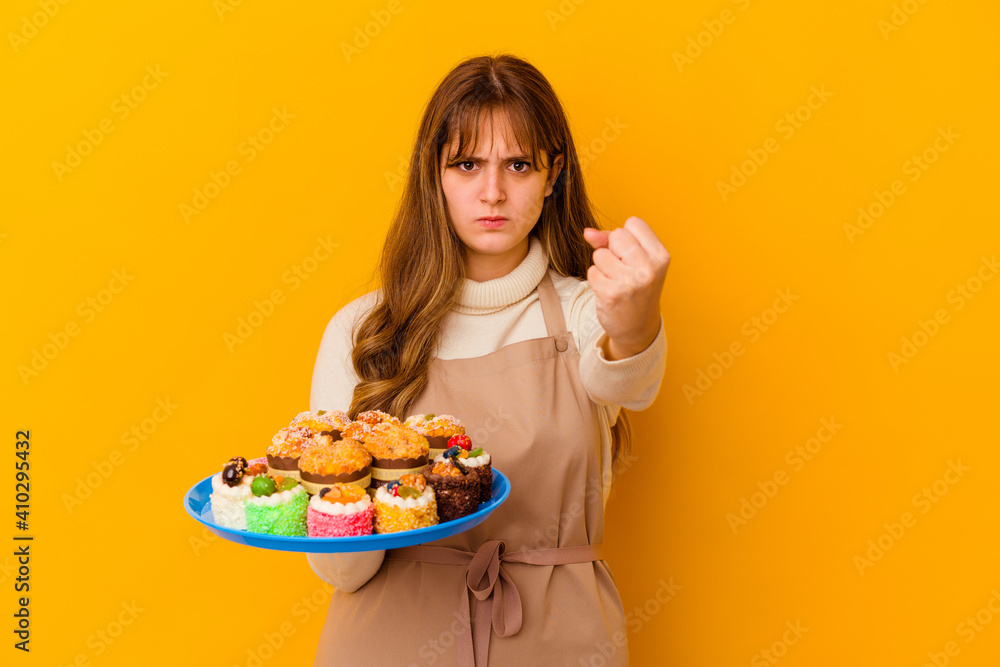 Young pastry chef woman isolated on yellow background showing fist to camera, aggressive facial expression. Young pastry chef woman isolated on yellow background showing fist to camera, aggressive facial expression.