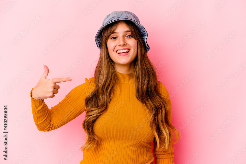 Young caucasian woman wearing fishermans hat isolated person pointing by hand to a shirt copy space, proud and confident - obrazy, fototapety, plakaty 