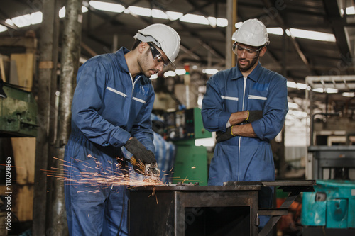 Fotografie, Tablou Young manual worker using grinder on metal in factory