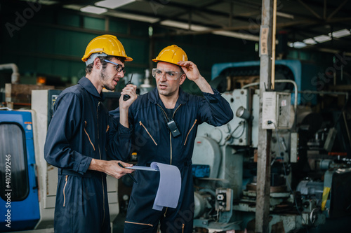 Two workers at an industrial. technician engineer checking process on notebook to machinery in factory. workers using machine equipment in factory