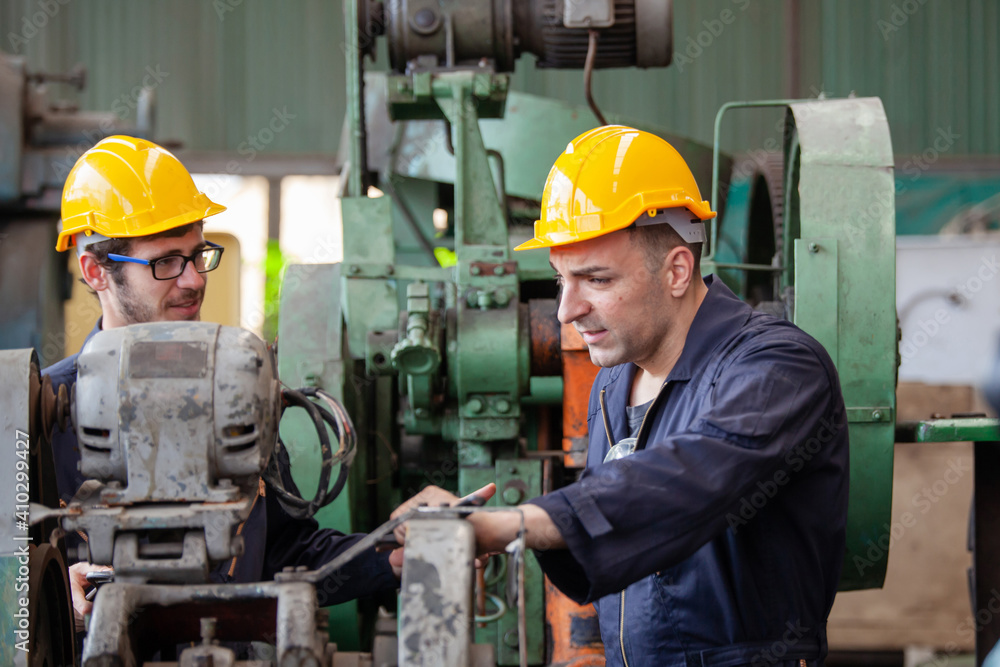 Two workers at an industrial. technician engineer checking process on notebook to machinery in factory. workers using machine equipment in factory Two workers at an industrial. technician engineer checking process on notebook to machinery in factory. workers using machine equipment in factory