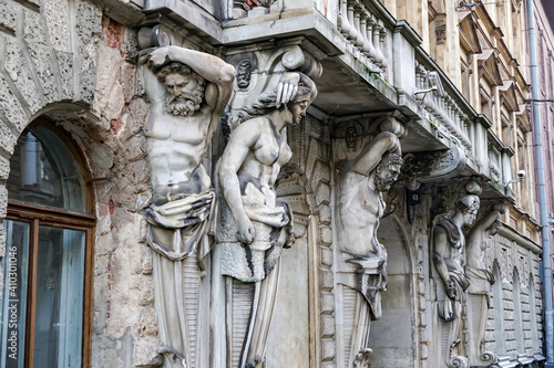 The statues of the stone Atlanteans, darkened by time, support the balconies of the old house, the antique architecture of St. Petersburg, the marks of restoration on the fingers and other elements photo