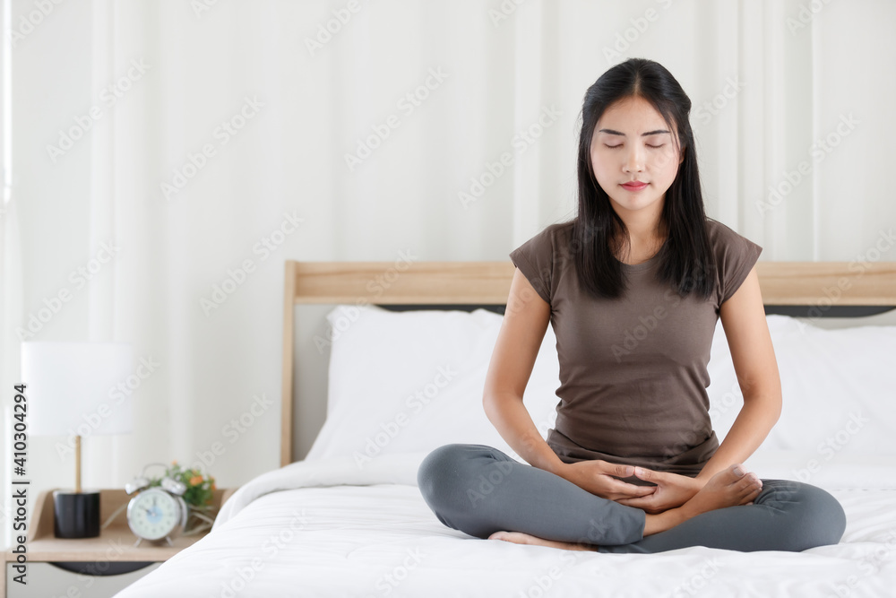 Female Buddhist sitting on bed in the bedroom and doing meditation in Buddhism religion style. The idea for faith and trust in religion and calm of mind Female Buddhist sitting on bed in the bedroom and doing meditation in Buddhism religion style. The idea for faith and trust in religion and calm of mind