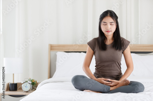 Female Buddhist sitting on bed in the bedroom and doing meditation in Buddhism religion style. The idea for faith and trust in religion and calm of mind