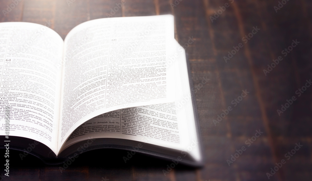 Fototapeta premium A Bible Open on a Rustic Wooden Table with Pages Blowing Open
