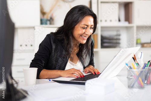 Картината върху платно Smiling successful hispanic business woman working on laptop in modern office