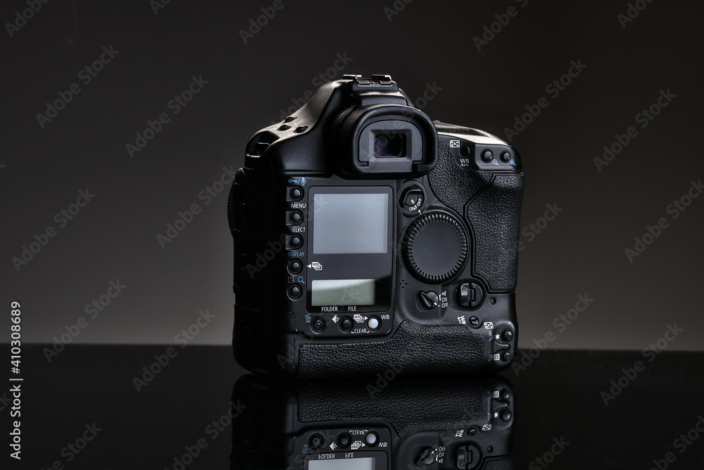 A black professional SLR camera sits on a glass table with a reflection. Advertising photo of the camera on a black background. Rear view. A black professional SLR camera sits on a glass table with a reflection. Advertising photo of the camera on a black background. Rear view.