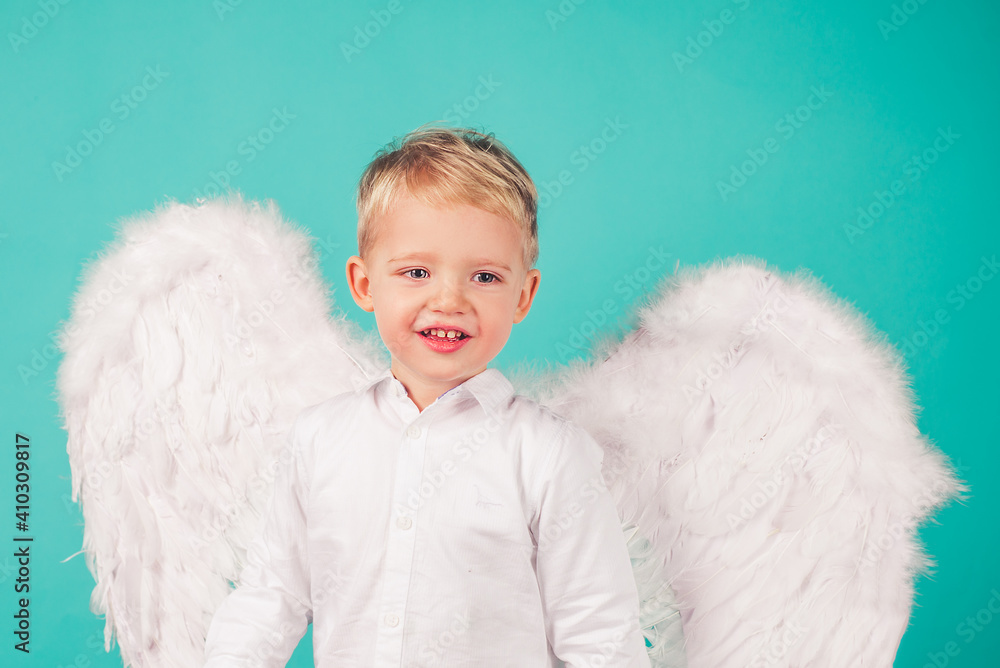 Portrait of little blond Angel boy. Child with angelic white dress. Toddler boy wearing angel costume, white dress and feather wings. Consept of innocent child. Portrait of little blond Angel boy. Child with angelic white dress. Toddler boy wearing angel costume, white dress and feather wings. Consept of innocent child.