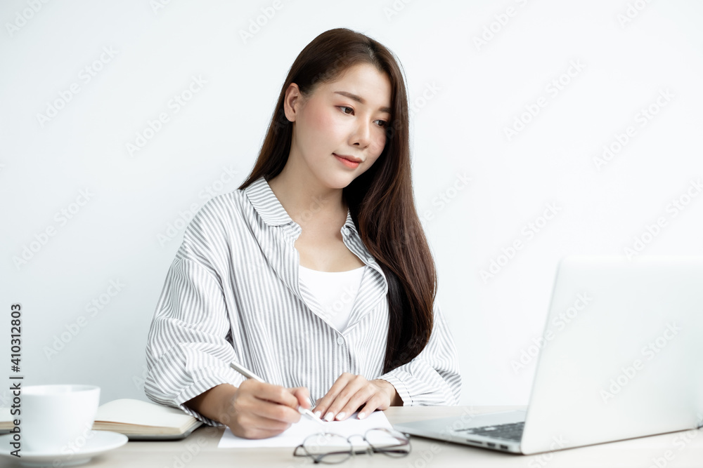 Asian female college students study online at home, enjoy extra lessons, watch videos, and take notes from a digital laptop, do homework by looking at the screen while sitting at a desk at home Asian female college students study online at home, enjoy extra lessons, watch videos, and take notes from a digital laptop, do homework by looking at the screen while sitting at a desk at home
