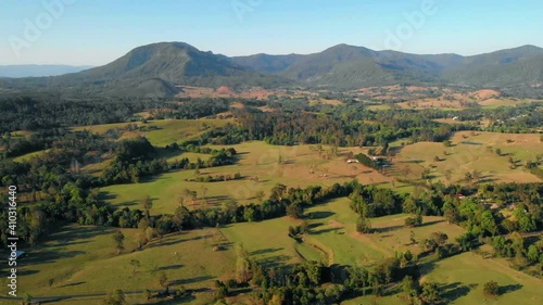 Aerial view of fields and trees, towards mountains, sunny day, on the countryside of Nimbin, Australia - dolly, drone shot photo