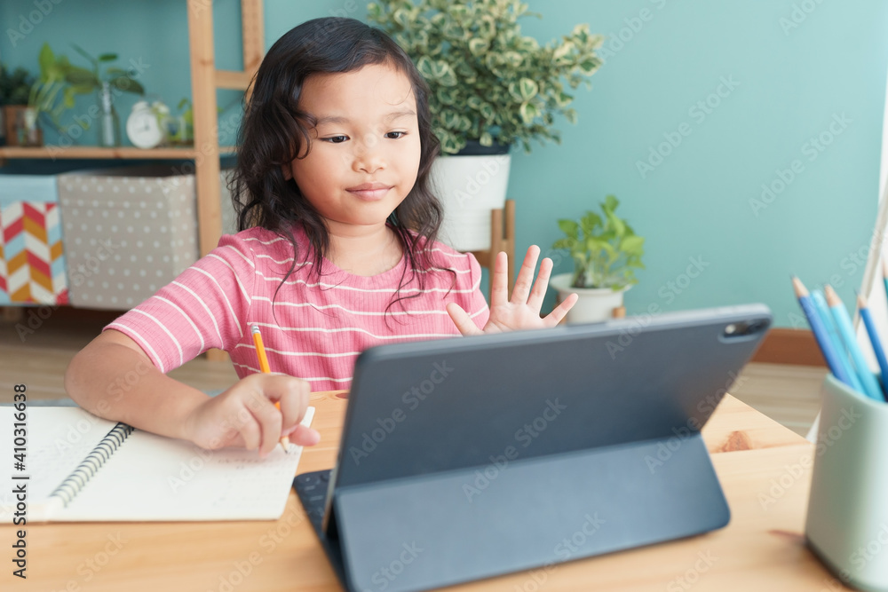 Asian little girl waving in greeting online tutor on tablet digital at home Asian little girl waving in greeting online tutor on tablet digital at home