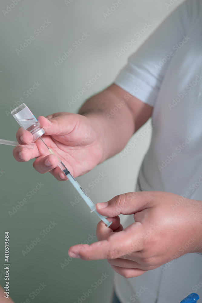 closeup to the hands of a latin man holding a syringe and medicinal liquid to be injected as a vaccine closeup to the hands of a latin man holding a syringe and medicinal liquid to be injected as a vaccine