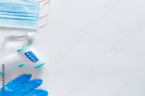 Corona virus protection concept flat lay. Non-contact infrared body thermometer, latex gloves, disposable masks and sanitizer on white background with copy space.