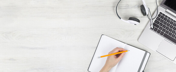 Laptop. keyboard and headphones on grey wooden desk. hand with pencil and notebook. Helpdesk or call center headset. Distant learning or working from home, online courses or support center concept.