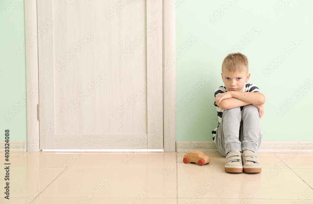 Sad little boy with wooden car sitting near closed door Sad little boy with wooden car sitting near closed door