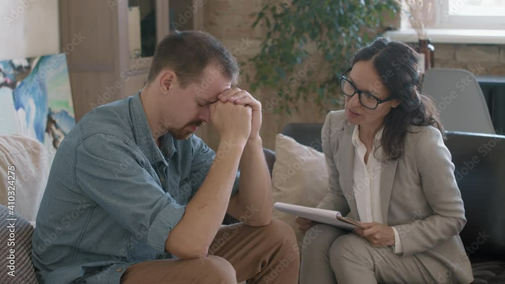 Medium shot of middle-aged female therapist with clipboard talking and supporting male client with depression Medium shot of middle-aged female therapist with clipboard talking and supporting male client with depression
