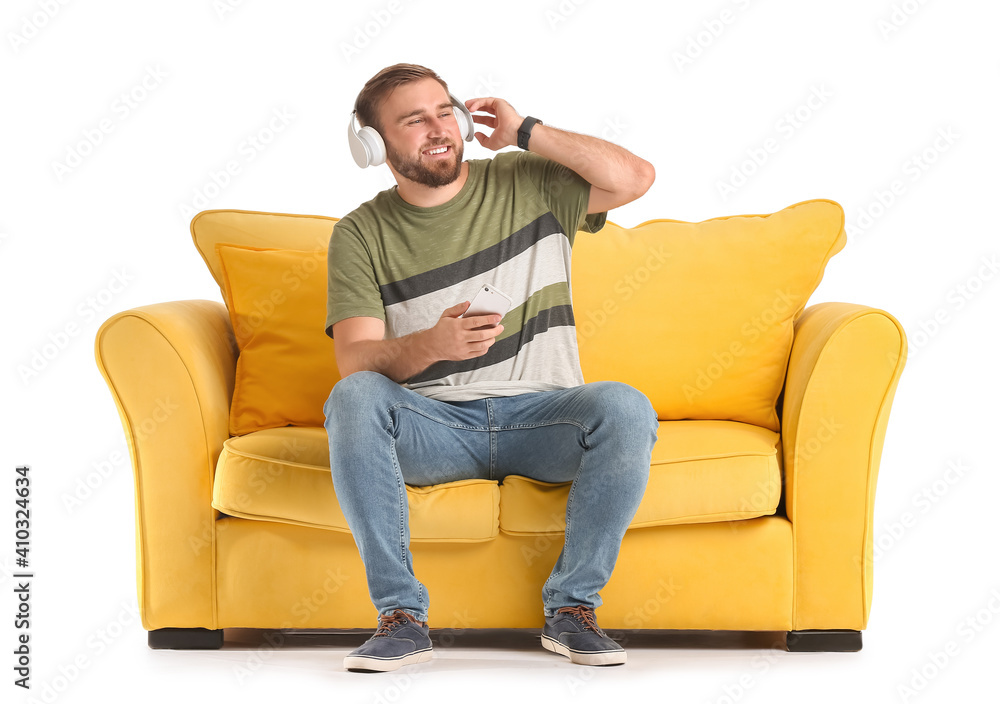 Young man with headphones and mobile phone on sofa against white background