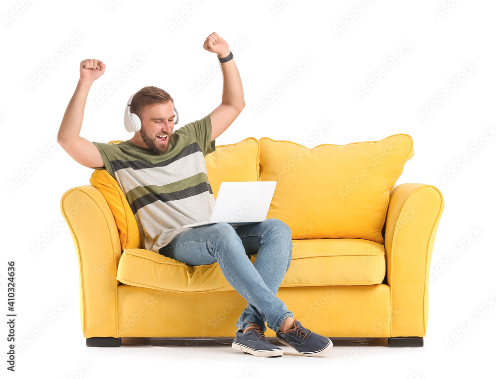 Happy man with headphones and laptop on sofa against white background Happy man with headphones and laptop on sofa against white background
