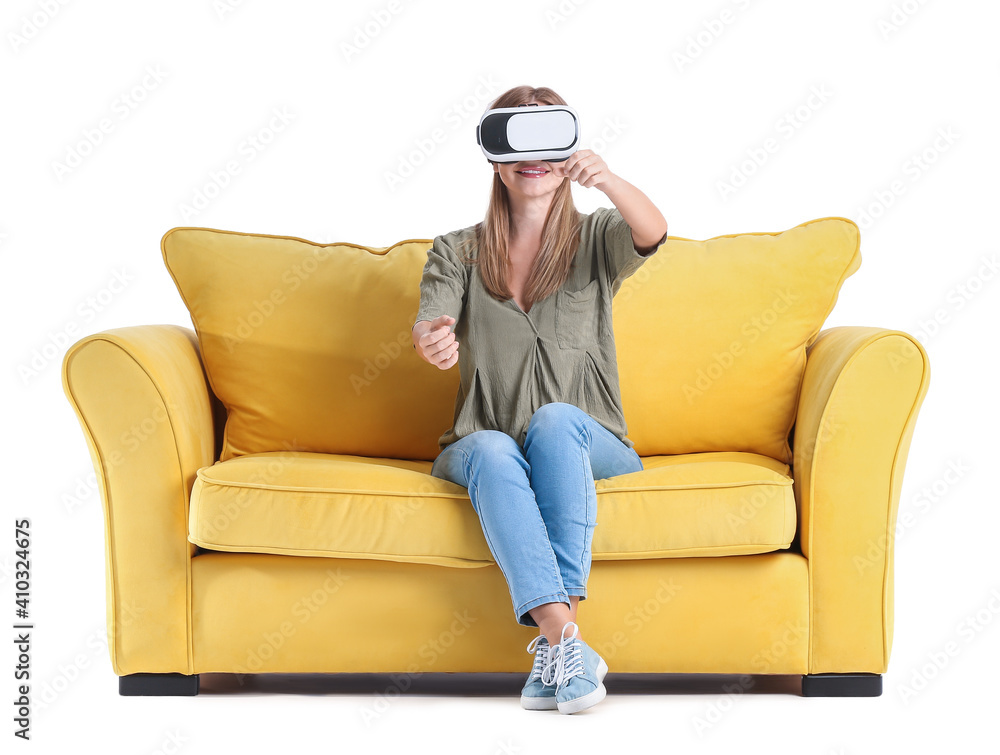 Young woman with virtual reality glasses on sofa against white background