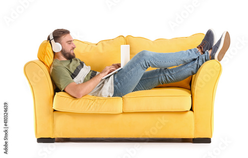 Young man with headphones and laptop on sofa against white background
