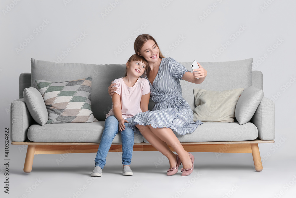 Mother and daughter taking selfie on sofa against light background