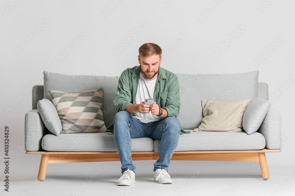 Young man with mobile phone on sofa against light background Young man with mobile phone on sofa against light background