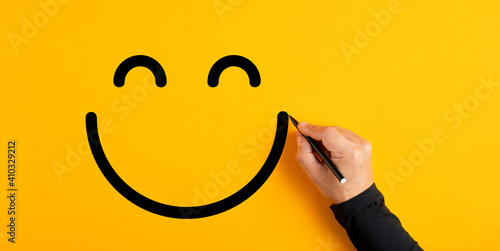 Male hand drawing a smiling happy face sketch on yellow background. Client satisfaction, service or product evaluation photo