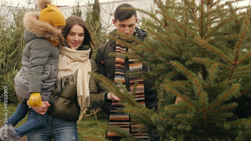 Family, winter holidays and people concept - happy mother, father and little daughter choosing christmas tree at street market.