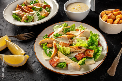 Chicken Caesar salad on a black background. Grilled chicken, romaine leaves, croutons and Parmesan, the classic recipe