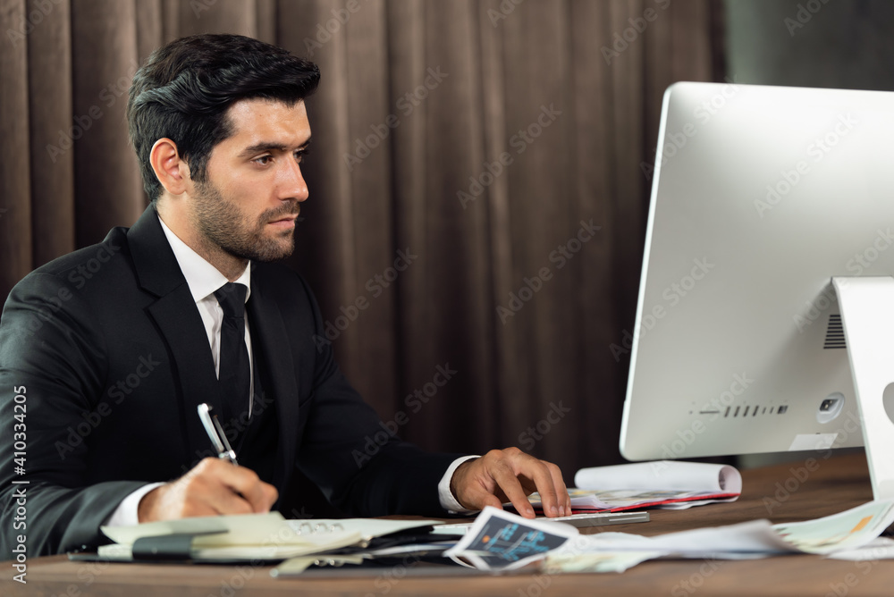 Portrait of young handsome confident businessman in suit working with desktop computer at office Portrait of young handsome confident businessman in suit working with desktop computer at office