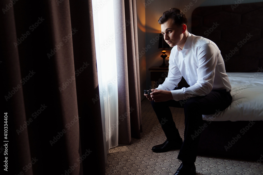 young man in a white shirt sitting on the bed and holding a bow tie young man in a white shirt sitting on the bed and holding a bow tie