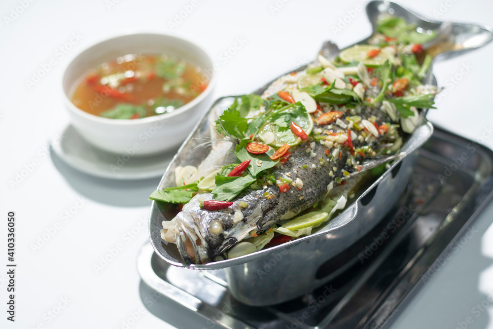 Plate of steamed Giant perch. Steamed fish with spicy lemon sauce on white background, Selective focus. Thai seafood for advertising ideas concept. Plate of steamed Giant perch. Steamed fish with spicy lemon sauce on white background, Selective focus. Thai seafood for advertising ideas concept.