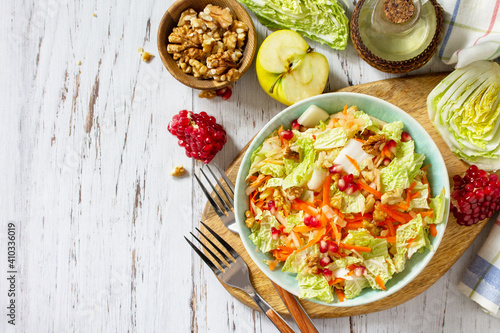 Dietary salad fresh vegetable of Chinese cabbage, carrots, apple, nuts and pomegranate with vinaigrette dressing on a white wooden table. Top view flat lay. Copy space.