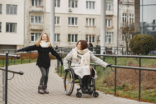 Disabled woman in wheelchair with daughter. Family walking outside at park.