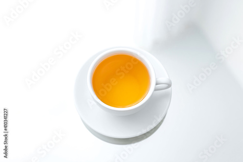 A horizontal photo of a white porcelain cup of green tea on a saucer, on a mirror table, a reflection