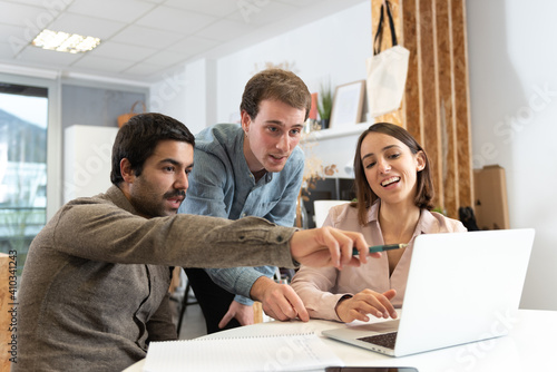 Three coworkers discussing and looking to a laptop.