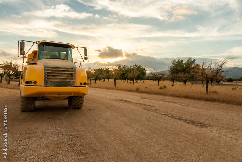 A dump truck parked on a construction site at sunset in a lonely field