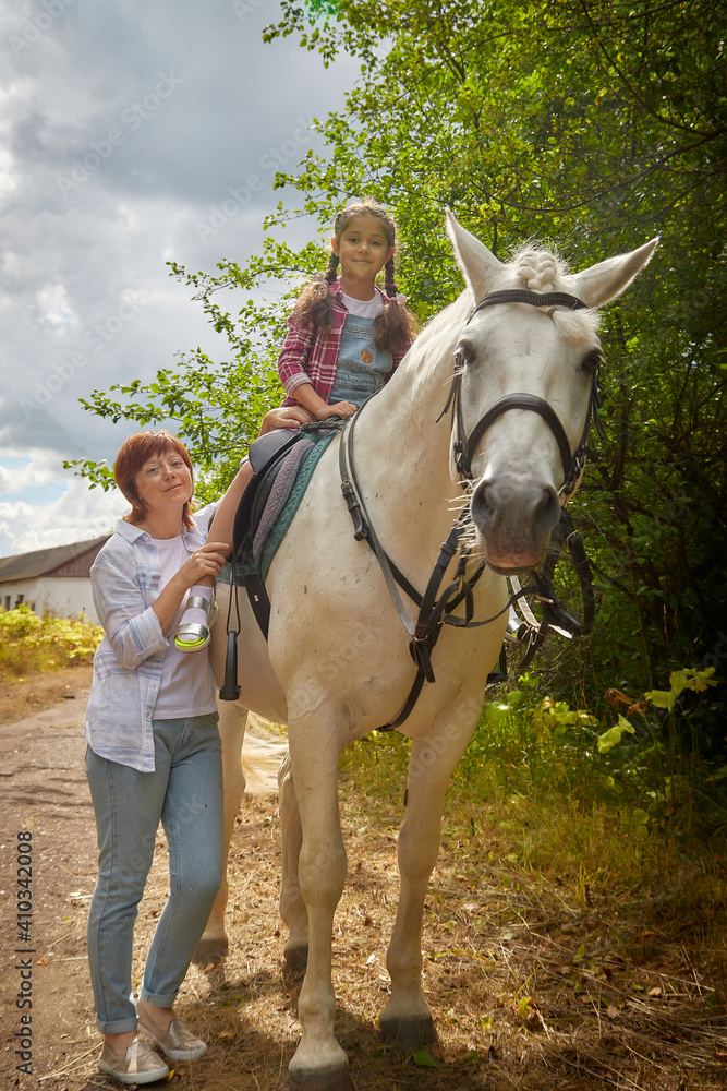 A teenage girl, mother and a horse in nature among green trees